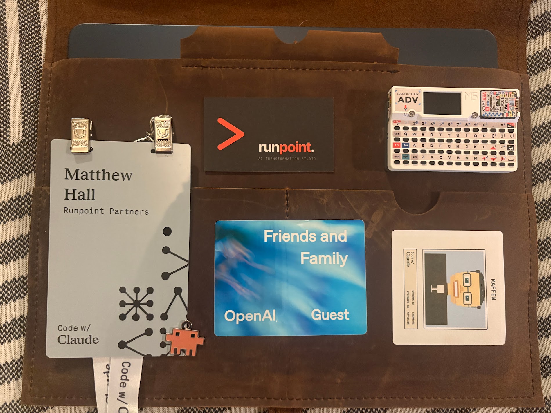 The Code w/ Claude folio, opened, with badge, business card, F&F pass, Cardputer, and MAFFEW trading card